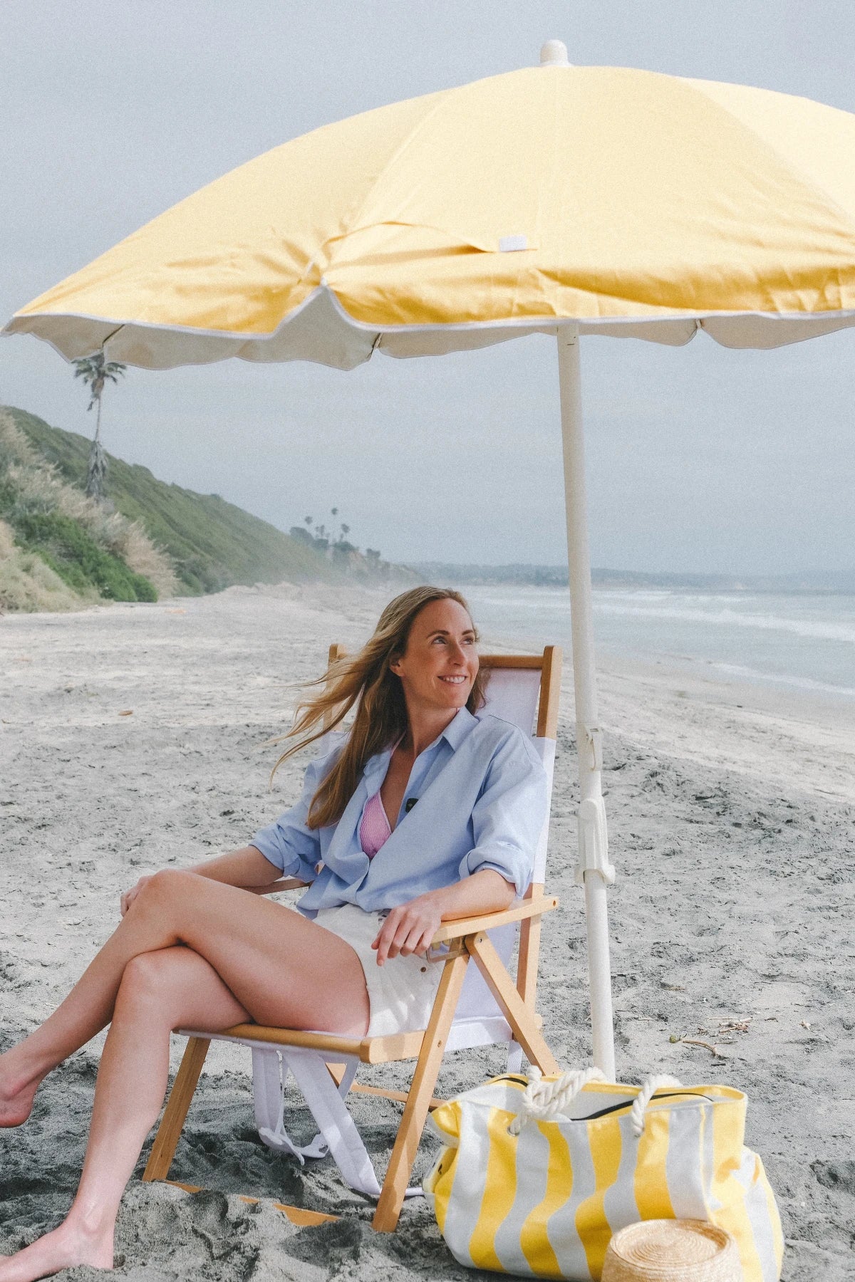 Brooke, founder of REYS, sitting under a yellow beach umbrella on the shore
