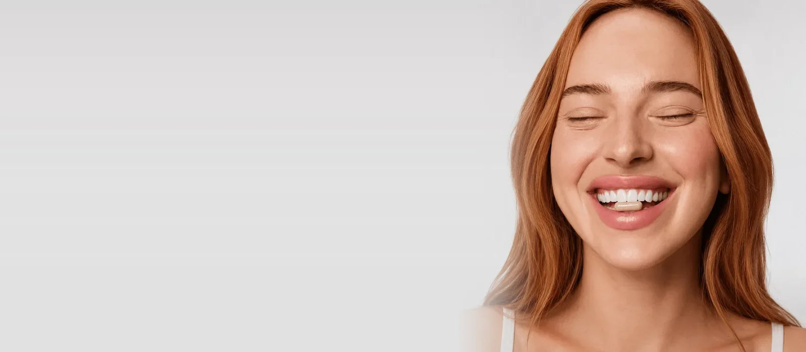 A smiling woman with a REYS capsule between her teeth